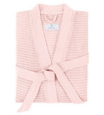The Kiran Robe by Matouk, shown folded with a matching belt on a white background, is crafted from luxurious light pink Turkish waffle fabric and features the Matouk label on the collar.
