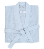 The Kiran Robe by Matouk is a folded light blue luxurious Turkish waffle fabric robe with a belt, shown from above.