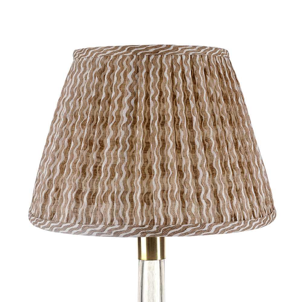 A close-up of the John Rosselli Fermoie Popple Nut Brown Lampshade, featuring a pleated fabric shade with brown and beige wavy stripes, shown mounted on a metallic stand.