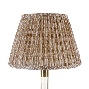 A close-up of the John Rosselli Fermoie Popple Nut Brown Lampshade, featuring a pleated fabric shade with brown and beige wavy stripes, shown mounted on a metallic stand.
