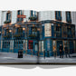 A spread from Laperouse: A Parisian Icon Since 1766 by Assouline shows a striking photograph of the iconic Paris restaurant—an ornate blue-and-white corner building adorned with gold trim, two figures at the entrance, and potted plants on its upper window ledges, alluding to its storied wine cellar within.