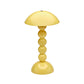 The Addison Ross Bobbin LED Cordless Lamp features a yellow, bobbin-shaped design with a dome shade and four stacked spheres as its base, offering adjustable brightness for versatile use, shown on a white background.