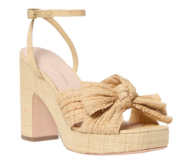 High-heeled sandal with a chunky cork platform, ankle strap, and a large braided bow over the toes by Loeffler Randall in a beige color.