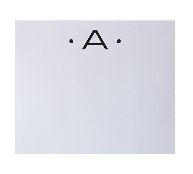 Centered on a white background, the Black Ink Black Initial Large Notepad features an uppercase "A" flanked by dots, showcasing refined elegance and quality craftsmanship for your stationery needs.