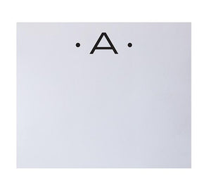 Centered on a white background, the Black Ink Black Initial Large Notepad features an uppercase "A" flanked by dots, showcasing refined elegance and quality craftsmanship for your stationery needs.