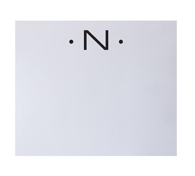 The Black Initial Large Notepad by Black Ink features a white background with a black capital "N" flanked by two dots at the top, recalling the elegance of fine stationery and suggesting luxurious quality paper.