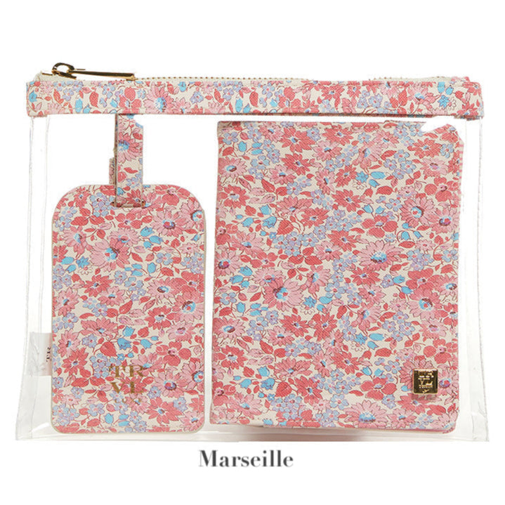 A clear zippered pouch showcases a floral LUXE Saffiano Travel Set by TRVL Design, featuring a matching luggage tag and passport cover in pink, blue, and white. "Marseille" appears below.