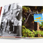 The open book, titled "La Colombe d'Or" by Assouline, displays on the left a black-and-white photo of people by a building. The right page features a vibrant sign of the same name, capturing Provençal's art de vivre with lush greenery and renowned modern art.