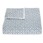 A folded white blanket from the Laksha Bedding Collection by Matouk, featuring a blue geometric dotted pattern inspired by Indian block printing and crafted from soft Luca percale, displayed on a plain white background.