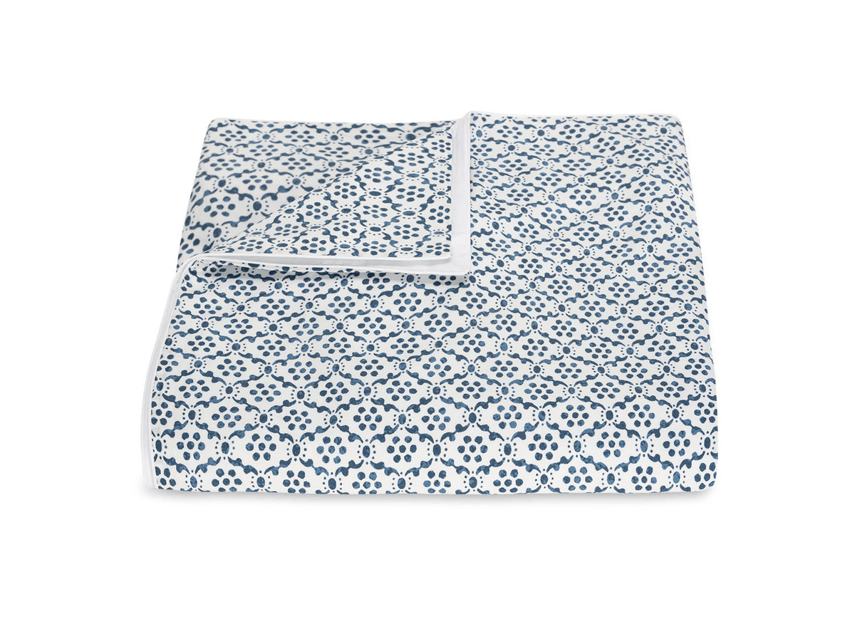 A folded white blanket from the Laksha Bedding Collection by Matouk, featuring a blue geometric dotted pattern inspired by Indian block printing and crafted from soft Luca percale, displayed on a plain white background.