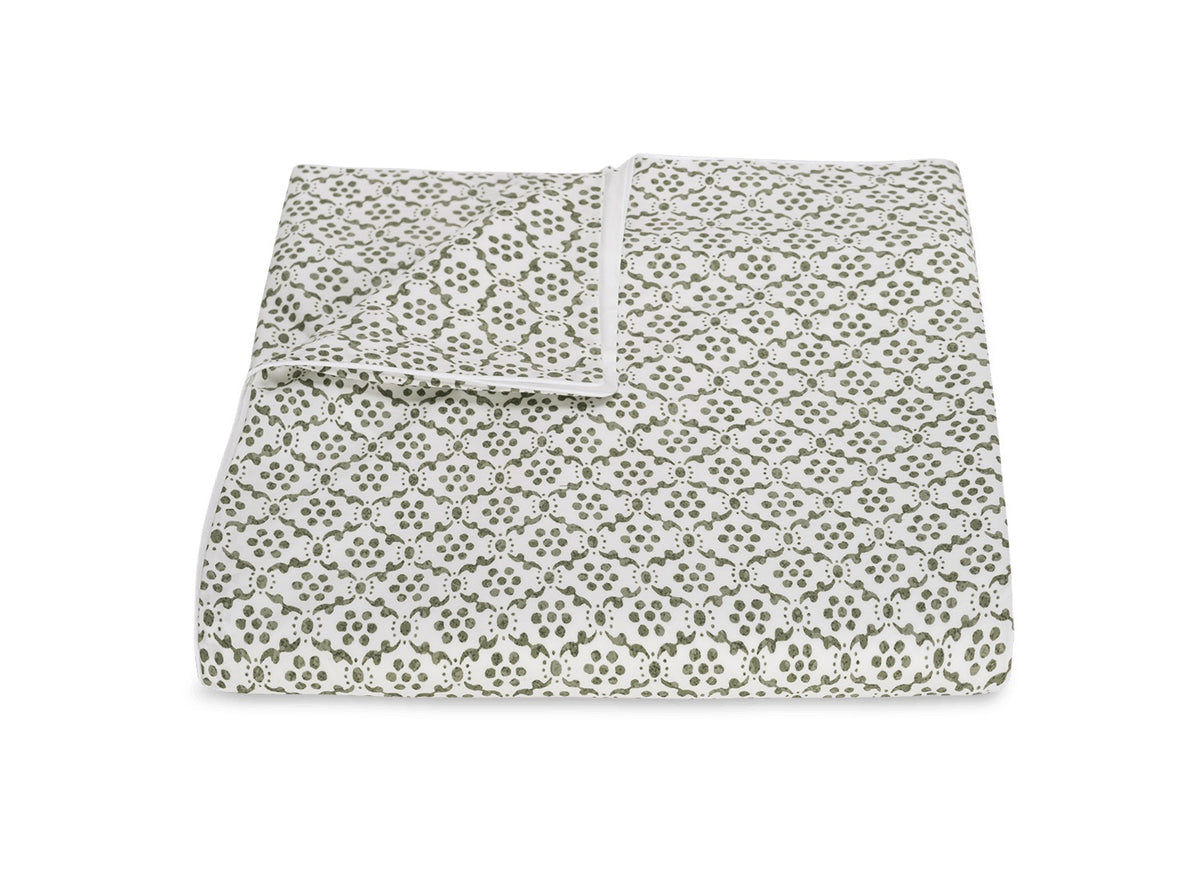 A folded blanket from the Laksha Bedding Collection by Matouk, featuring a small repeating green and white floral pattern inspired by Indian block printing, displayed against a plain white background.