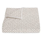 A folded quilt from the Laksha Bedding Collection by Matouk, showcasing a beige and white dotted geometric pattern inspired by Indian block printing, displayed on a white background.