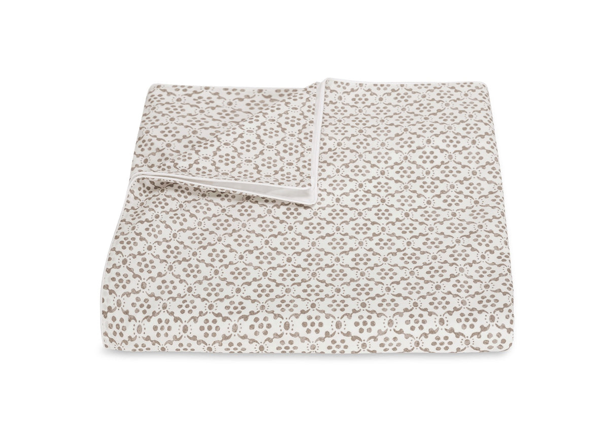 A folded quilt from the Laksha Bedding Collection by Matouk, showcasing a beige and white dotted geometric pattern inspired by Indian block printing, displayed on a white background.