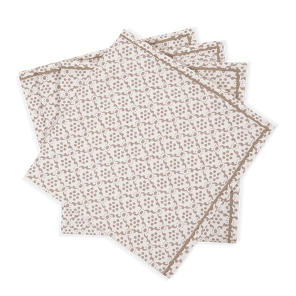 The Laksha Napkin Set by Matouk features four beige cloth napkins adorned with a delicate brown geometric pattern, reminiscent of block printing, artfully fanned out against a plain white background.
