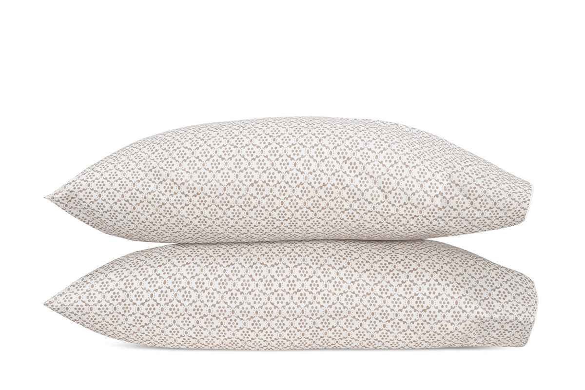 Two white pillows from the Matouk Laksha Bedding Collection, featuring a beige geometric pattern inspired by Indian block printing, are stacked one atop the other against a plain white background.