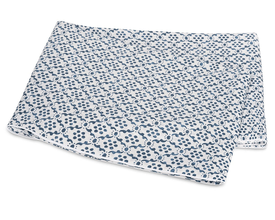 Folded white fabric from the Matouk Laksha Bedding Collection, featuring a repeating blue dot and line pattern inspired by Indian block printing, displayed on a white background.