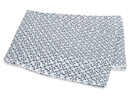 Folded white fabric from the Matouk Laksha Bedding Collection, featuring a repeating blue dot and line pattern inspired by Indian block printing, displayed on a white background.