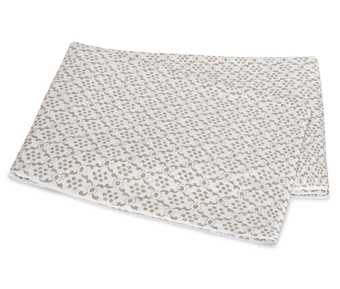 A folded white blanket from the Laksha Bedding Collection by Matouk, featuring a beige dot and line pattern inspired by Indian block printing techniques, displayed on a plain white background.