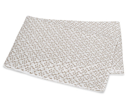 A folded white blanket from the Laksha Bedding Collection by Matouk, featuring a beige dot and line pattern inspired by Indian block printing techniques, displayed on a plain white background.