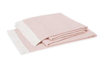 The Matouk Leo Throw is an oversized folded herringbone blanket in pink and white with a white fringe on one end, shown on a white background. This contemporary throw adds style and comfort to any space.