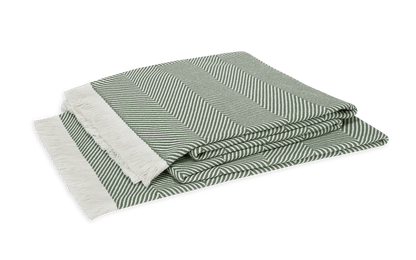 The Matouk Leo Throw, featuring an oversized green and white herringbone pattern with white fringe on one end, is displayed against a white background.