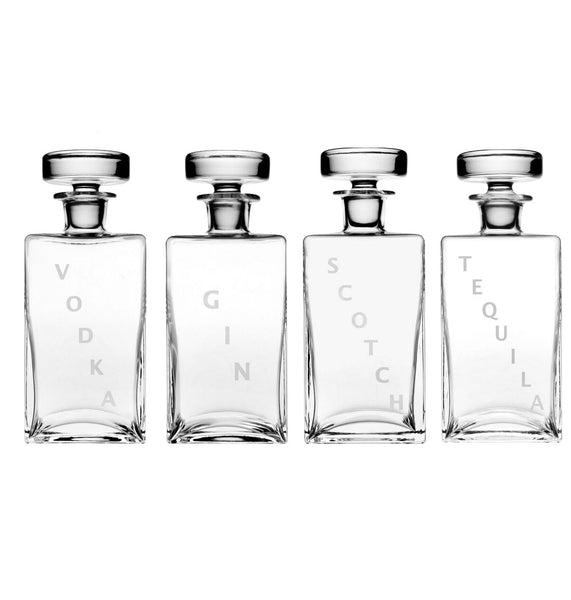 Four handmade crystal glass bottles are arranged in a row, each labeled vertically: "Vodka," "Gin," "Scotch," and "Tequila." These exquisite spirit decanters from the William Yeoward Crystal Lillian Square Decanter Collection by William Yeoward Crystal add a touch of elegance to any bar setup.