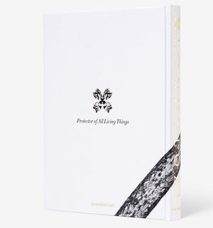 Assouline’s “Londolozi: The Safari that Changed Everything” is a white hardcover book featuring a black emblem, the phrase “Protector of All Living Things,” and a tree bark pattern evoking wilderness, conservation, and community development.