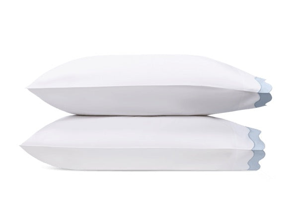 Two white pillows from the Matouk Lorelei Bedding Collection, crafted from luxurious 600 thread count Egyptian cotton and accented by delicate light blue appliqué scallop edges, are stacked together against a plain white background.