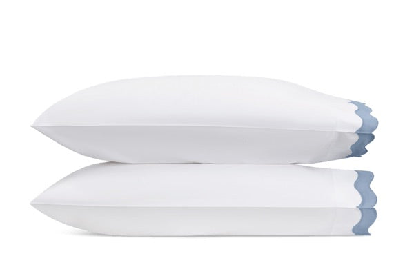 Two white pillows from the Lorelei Bedding Collection by Matouk, crafted from luxurious 600 thread count Egyptian cotton and featuring elegant blue appliqué scallop edges, are stacked on top of each other against a plain white background.