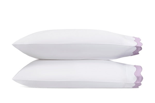 Two white pillows from the Lorelei Bedding Collection by Matouk, featuring purple appliqué scallop edges and crafted from luxurious 600 thread count Egyptian cotton, are stacked horizontally against a plain white background.