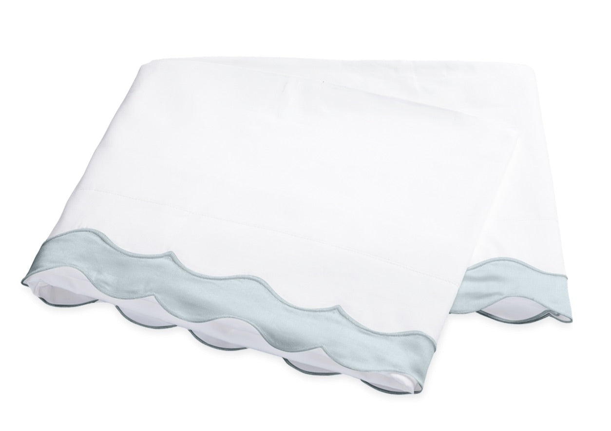Two folded white pillowcases from the Matouk Lorelei Bedding Collection, featuring light blue appliqué scallop edging and crafted from luxurious 600 thread count Egyptian cotton, are stacked on a white background.