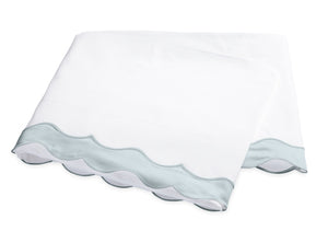 Two folded white pillowcases from the Matouk Lorelei Bedding Collection, featuring light blue appliqué scallop edging and crafted from luxurious 600 thread count Egyptian cotton, are stacked on a white background.