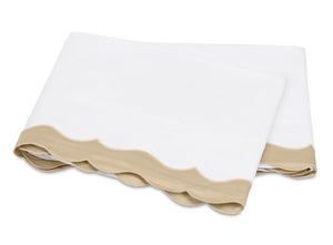A folded white bedsheet from the Matouk Lorelei Bedding Collection, featuring an appliqué scallop beige edge and crafted from luxurious 600 thread count Egyptian cotton, is displayed against a plain background.