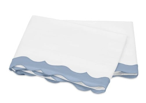 Experience the Lorelei Bedding Collection by Matouk: two folded sheets in white, featuring appliqué scallop blue edges and expertly crafted from 600 thread count luxurious Egyptian cotton.