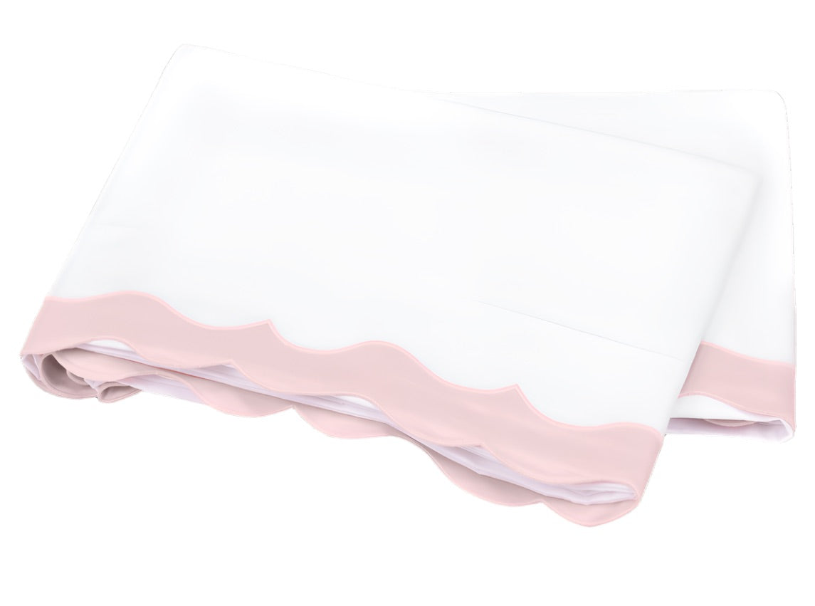 A folded white bed sheet from the Lorelei Bedding Collection by Matouk, featuring a pink appliqué scallop edge and crafted from luxurious 600 thread count Egyptian cotton, displayed on a white background.