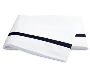 Two folded white pillowcases from the Matouk Lowell Bedding Collection in Navy, crafted from 600 thread count Egyptian cotton percale with a single navy stripe near the edge, are displayed on a plain background.