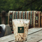 Baobab Collection Halona White World Candle, a hand-blown glass candle holder with a brown and white marbled pattern and a square logo label, sitting on a wooden table.