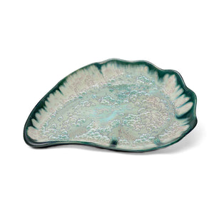 The Large Oyster Plate Collection by AE Ceramics features a ceramic serving platter with an abstract leaf shape, scalloped edges, and a green-blue glazed pattern.