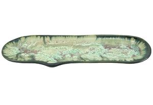 The Large Razor Clam Tray Collection by AE Ceramics features a long, oval ceramic platter with a glossy green, beige, and brown mottled glaze, inspired by coastal dinnerware and hand-molded razor clam plates.