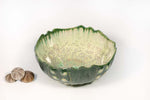 A green wavy-rimmed bowl from AE Ceramics’ handmade Sea Urchin Bowl Collection sits beside three small seashells on a white background.