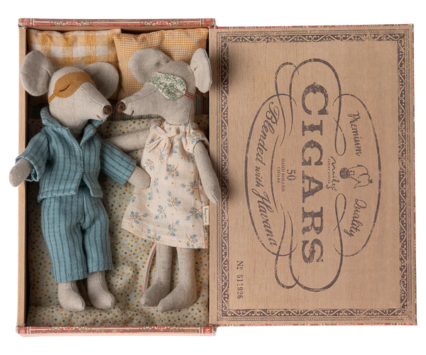 Two Maileg Mum & Dad Mice in nightwear lie in a small, vintage-style cigar box bed with a pillow and blanket from the brand Maileg.