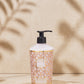 The Baobab Collection Women Body Wellness Collection by Baobab, featuring a geometric-patterned bottle with pump dispenser, rests on a round tray against a beige backdrop with leaf shadows, suggesting a subtle floral fragrance.