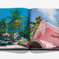 The Mustique Icon by Assouline features an open book showcasing a vivid scene of palm trees, colorful boats, and pink-roofed houses, capturing Caribbean luxury on the exclusive private island of Mustique.