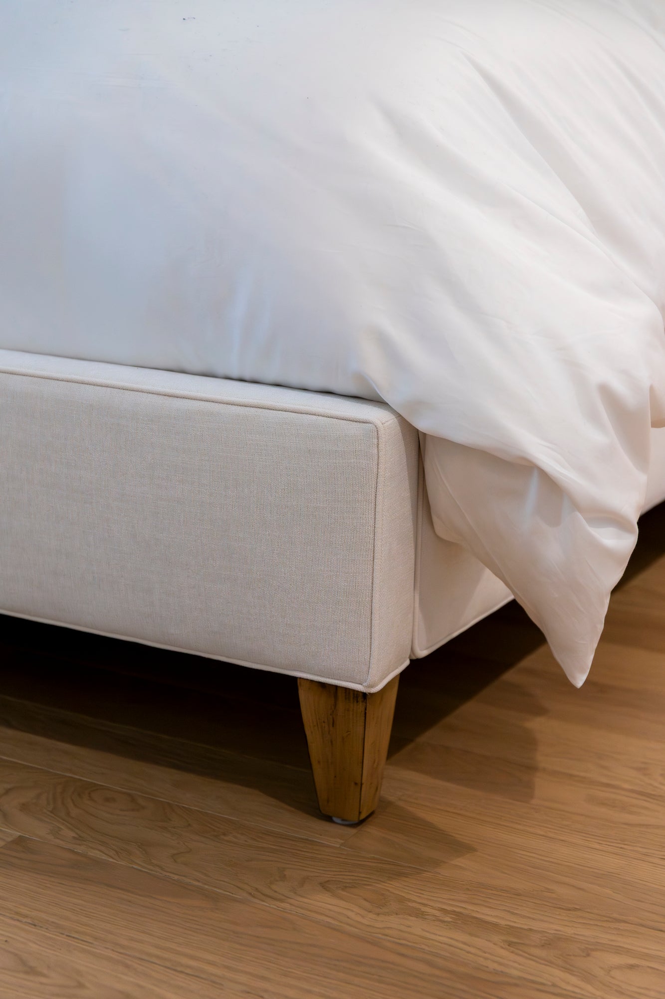 Close-up of the Laguna Cloud Cut Corner King Bed by Lee Industries, featuring a modern upholstered design with wooden legs and a white comforter, set on a wooden floor for contemporary elegance.