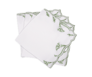 A set of four Marcella Napkins by Matouk, featuring white fabric with green embroidered leaf motifs and scalloped edges, displayed fanned out on a white background.