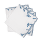 A set of four Marcella Napkins by Matouk, featuring white cloth with scalloped edges and blue embroidered leaf patterns, neatly stacked in a fanned arrangement on a white background.