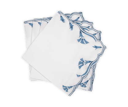A set of four Marcella Napkins by Matouk, featuring white cloth with scalloped edges and blue embroidered leaf patterns, neatly stacked in a fanned arrangement on a white background.