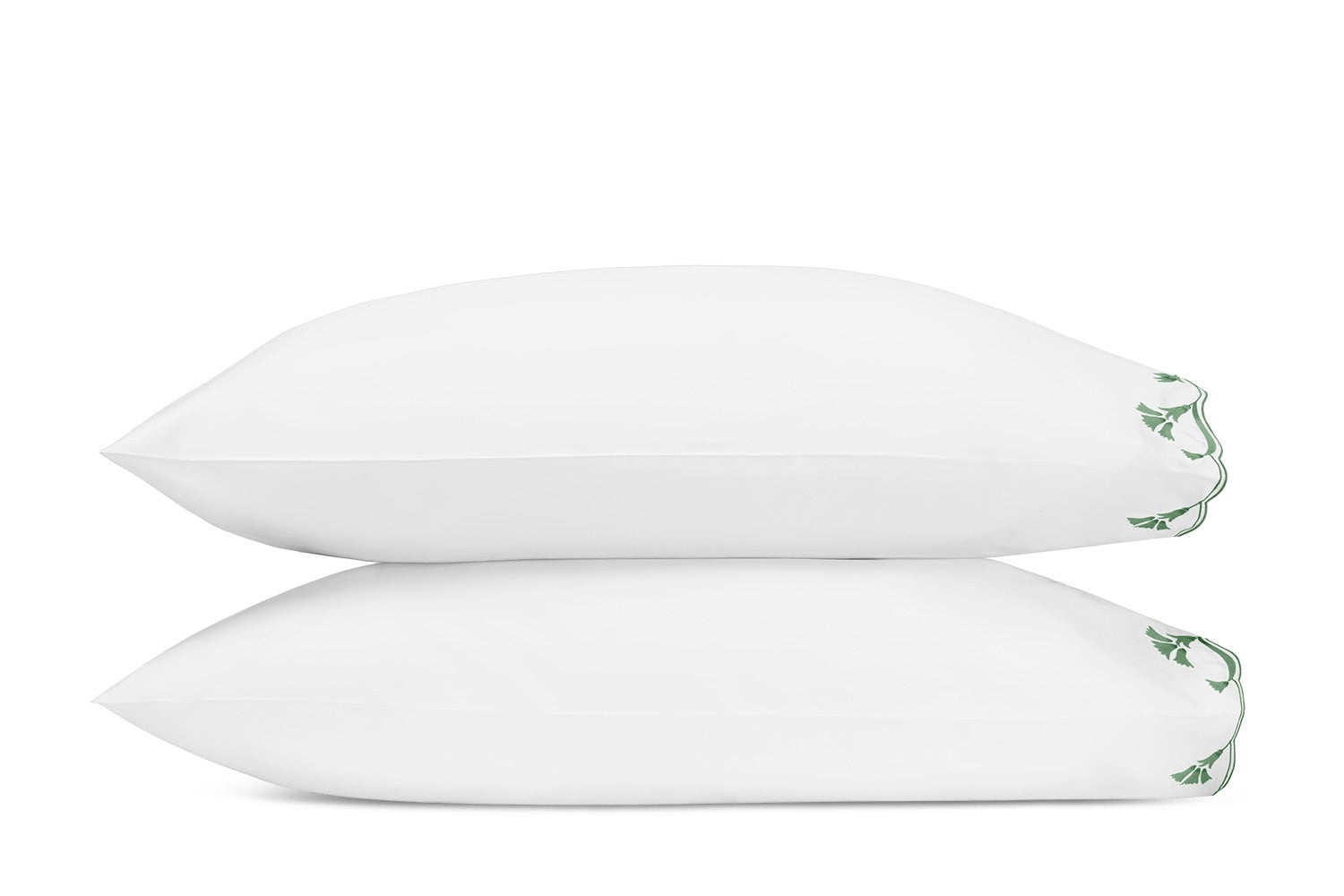 Two white pillows from the Marcella Bedding Collection by Matouk are stacked horizontally, each featuring a green leaf embroidered detail on the corners, set against a plain white background.
