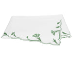 A folded white handkerchief with scalloped florals and delicate green embroidery, reminiscent of the Marcella Bedding Collection by Matouk, is placed on a white background.