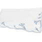 A folded white cloth napkin with scalloped edges and delicate light blue floral embroidery in one corner, echoing the signature scalloped florals of Matouk’s Marcella Bedding Collection.